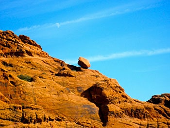 St. George, Utah: Red Rocks Calling 7 A boulder balances on the edge of a mountain as the daytime moon illuminates the sky.