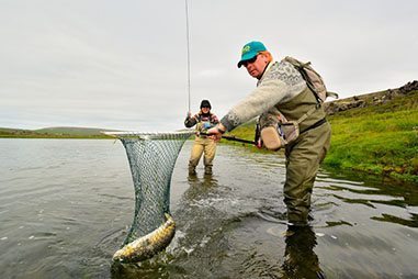 Two men work together to catch a fish on Lake Thingvallavatn.