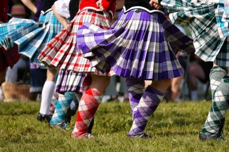 A Highland Dance costume consists of: tartan sock and kilt, velvet jacket with a lace insert, or a sleeveless velvet vest worn over a white blouse.