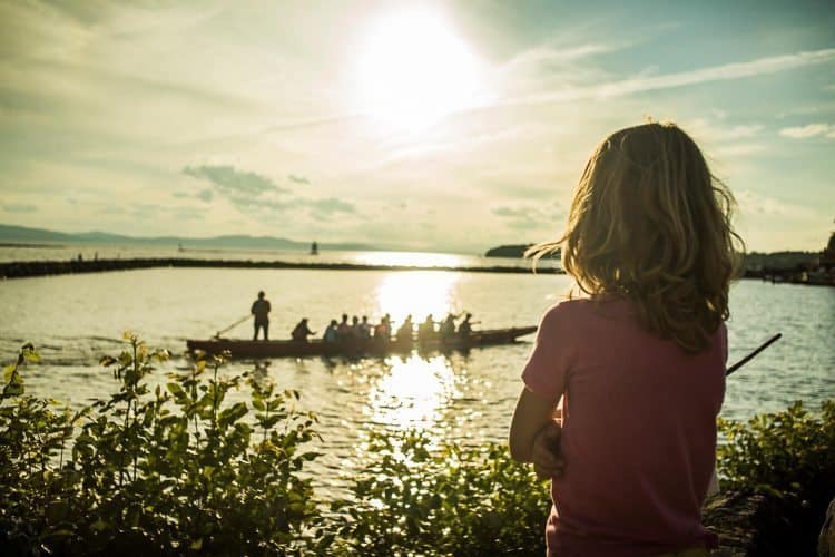 A young girl watches a boat pass by at the waterfront stage.