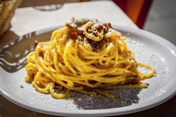 Pasta Alla carbonara twisted into a perfect spiraling mound, so yellow, glistening with eggs and cheese, topped with pieces of guanciale (thick bacon). Creamy, salty, al dente perfection.