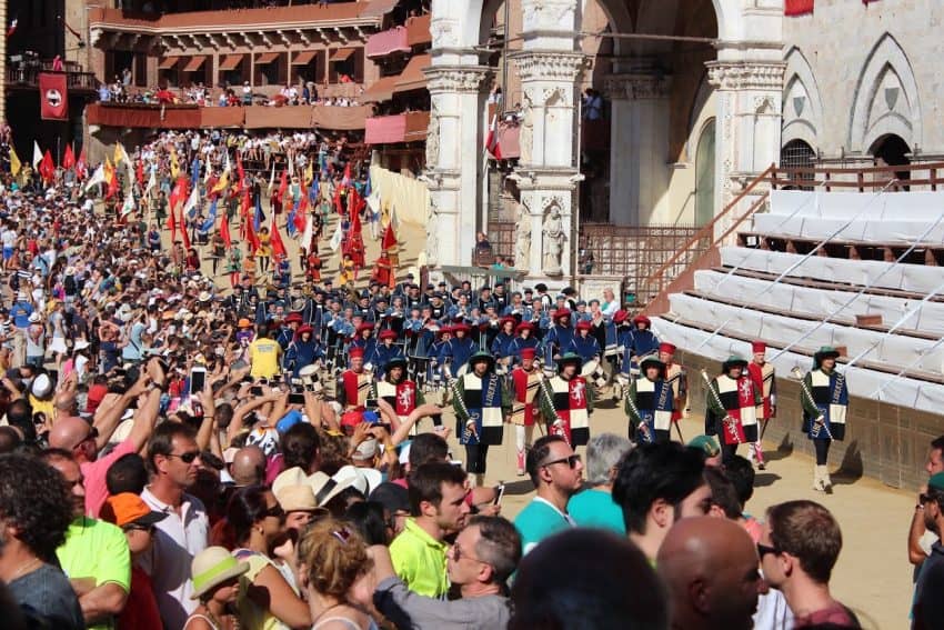 Musicians and a color guard march along the track in historical Sienese outfits.