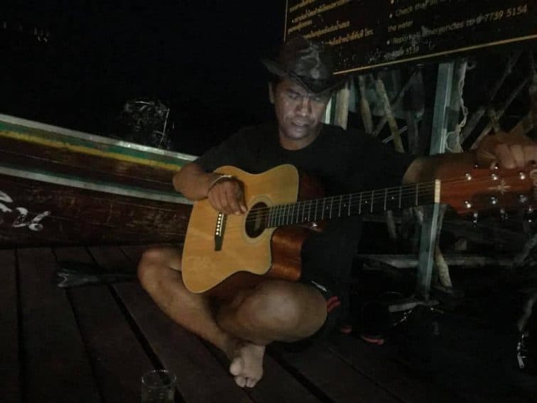 A tour guide plays guitar in the evening on Chiaw Laan Lake, Thailand. | GoNOMAD Travel