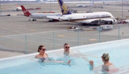 Guests wade in the heated rooftop pool with a Singapore Airlines A380 in view.