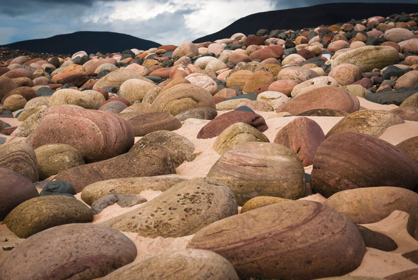 The beach at Rackwick Bay. Marine erosion and weathering have rounded these boulders, which highlights the sedimentary layers of Old Red Sandstone. The larger boulders weigh as much as 300kg (660lbs) and give an indication of the power of waves during storm conditions.