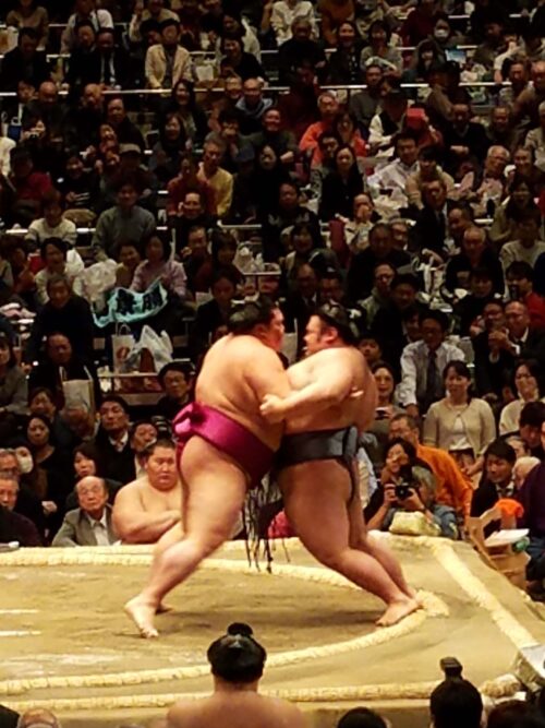 Wrestlers clash with mighty shoves and throws in pushing their opponent out of the ring or to the floor, Tokyo, Japan;