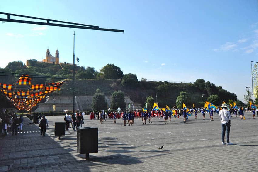 Cholula: Mexico's Very Big Archaeological Site 1 The Great Pyramid of Cholula rises behind a town plaza where groups prepare for a Cinco de Mayo parade.
