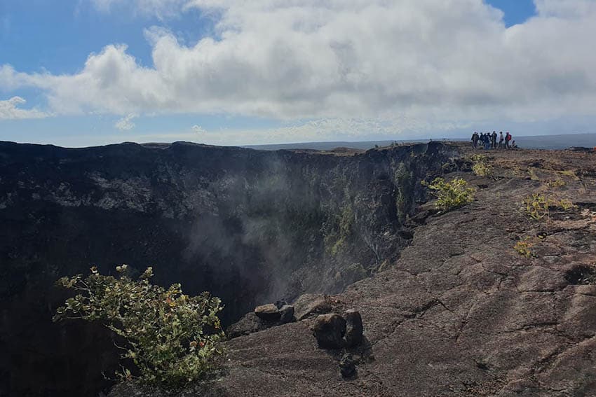 The incredibly deep Maunaulu Crater crater venting gas as a group of hikers peer into its depthsImage credit: Charlie Winchester & Kate Dziubinska