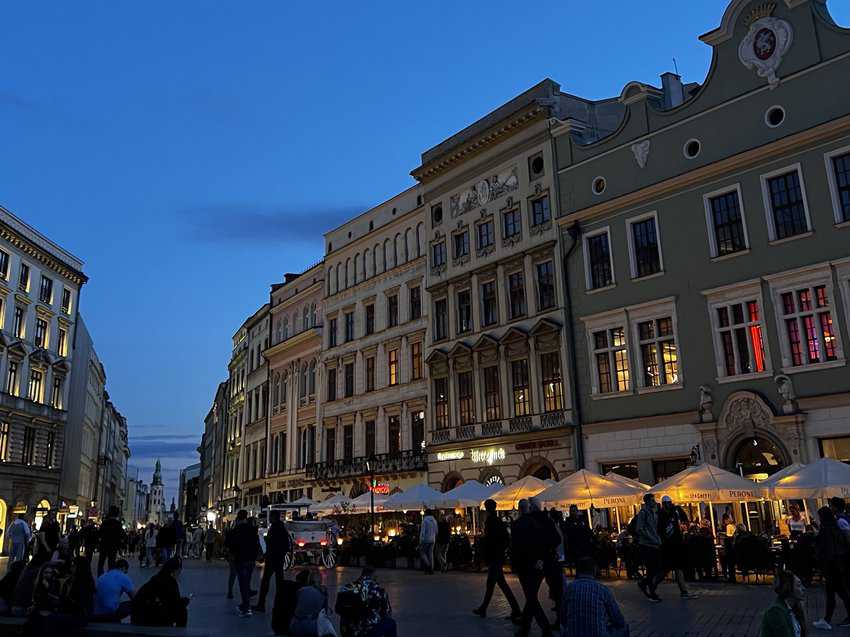 The enchanting city center of Krakow at dusk, illuminated by the warm glow of streetlights, accompanied by the melodic tunes of live musicians.