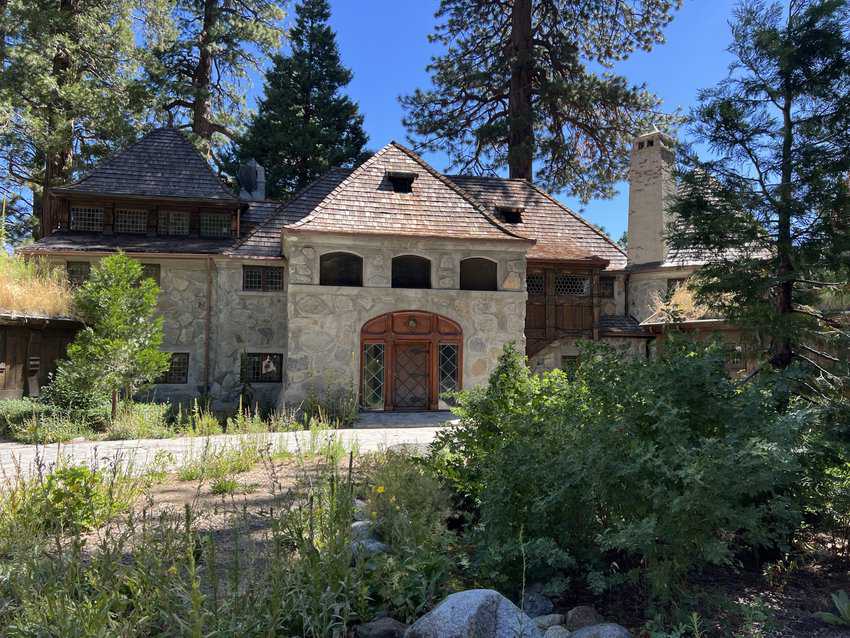 North Lake Tahoe, California 11 Stone house with large wooden door in front of a drive surrounded by greenery and pine trees.