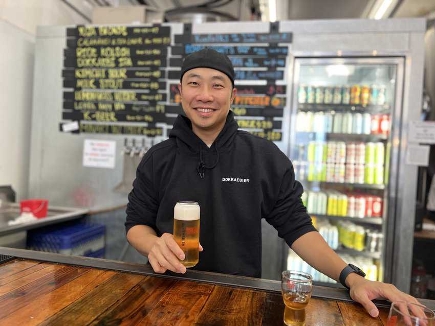 Oakland: Discover the City's Unique Neighborhoods and Cultural Heritage 12 An image of Youngwon Lee, founder of Dokkabier Craft Brewery, holding a beer in his hands in front of the counter at Jack London Square.