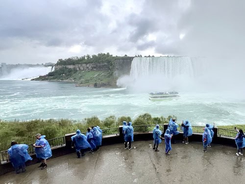 a group of people in blue raincoats standing on a ledge overlooking a waterfall